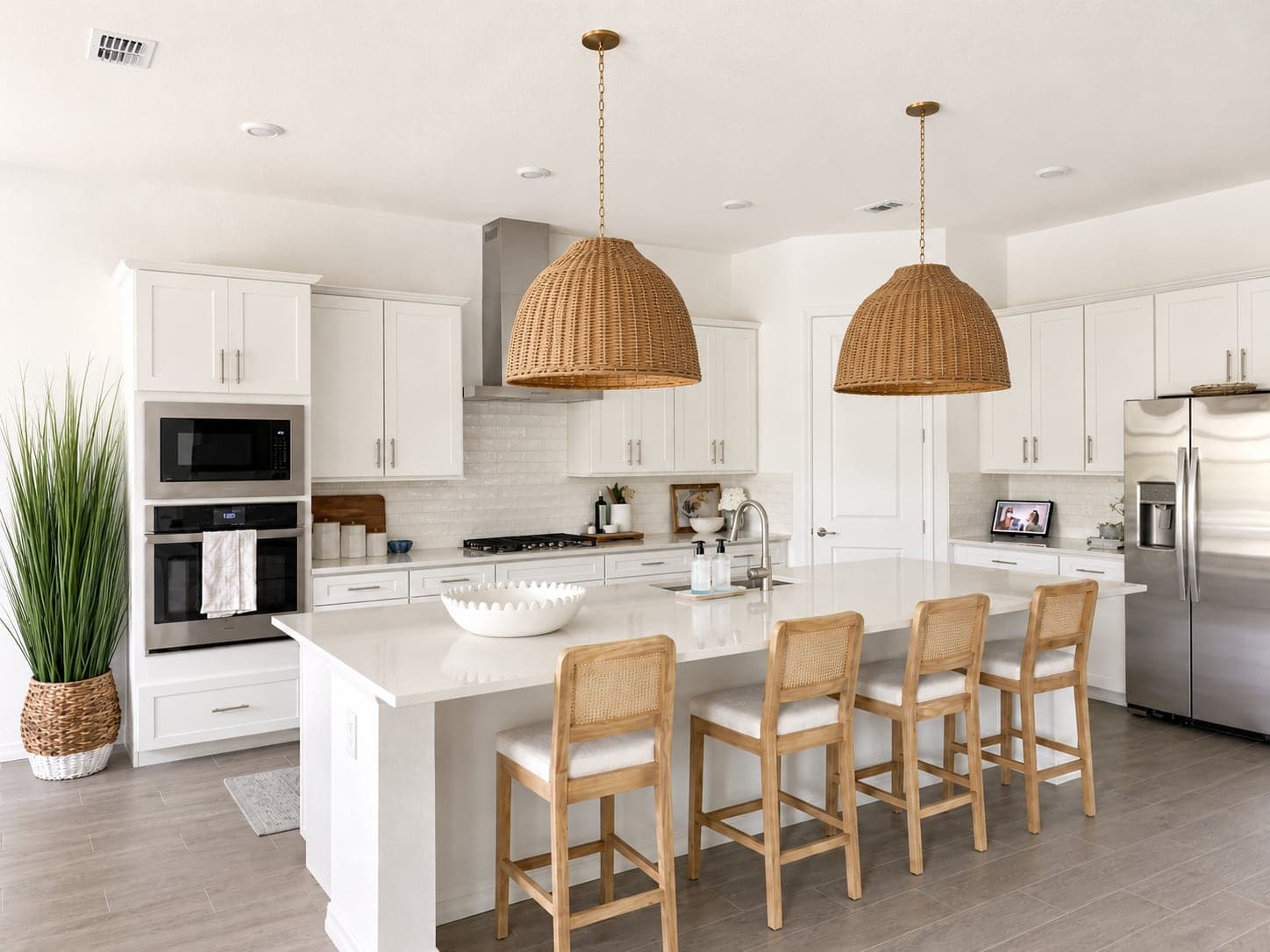 White kitchen with woven dome pendants, a quartz island, and cane counter stools